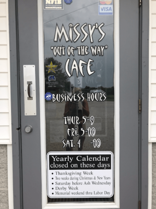 Sign on a door displaying "Missy's 'Out of the Way' Cafe" with business hours and holiday closures.