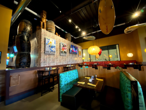 Interior of a vibrant restaurant featuring colorful decor, wooden barrels, and cozy seating with tropical themes.