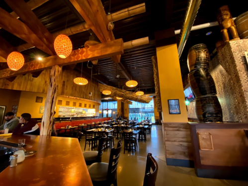 Interior of a cozy restaurant featuring wooden beams, warm lighting, and a bar area with tables set for dining.