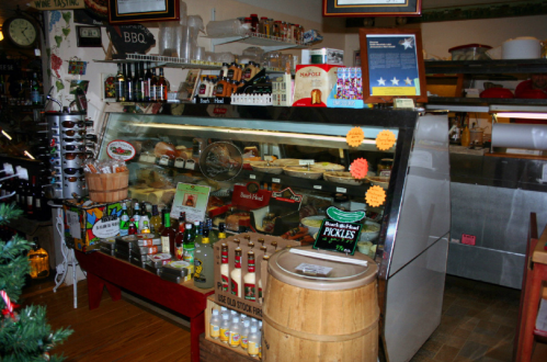 A display case filled with various food items, including meats and pickles, in a cozy shop setting.