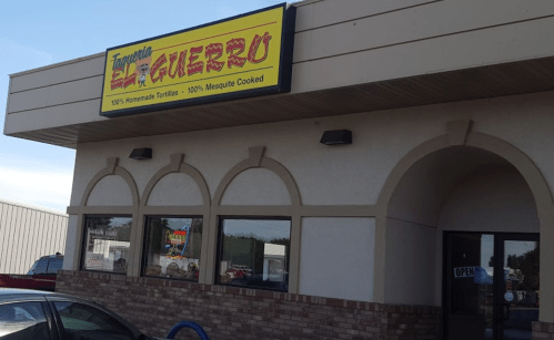 Exterior of Taqueria El Guerrero, featuring a bright sign and a welcoming entrance, with a clear blue sky above.