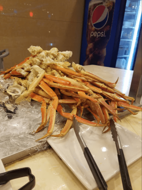 A pile of crab legs on ice, with a pair of tongs resting beside them, and a Pepsi vending machine in the background.