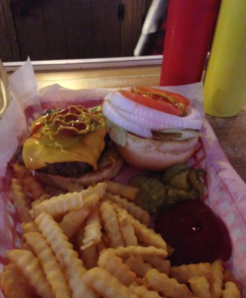 A plate with a cheeseburger topped with ketchup and mustard, a plain bun, and a side of crinkle-cut fries.