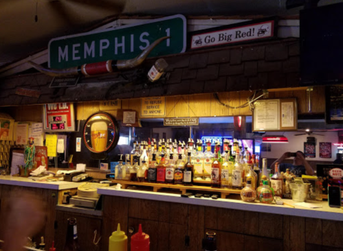 A bar counter with various bottles of liquor, condiments, and a sign reading "Memphis" in a casual setting.