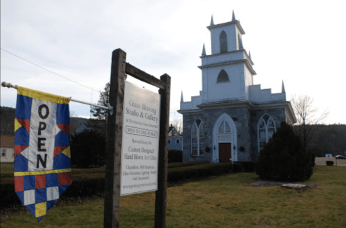 A historic church building with a sign reading "OPEN" in front, surrounded by grass and trees.