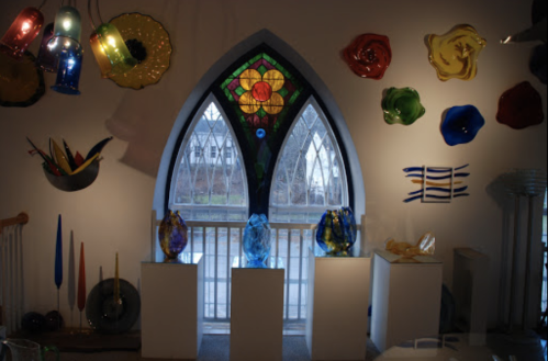 Colorful glass art displayed in front of a stained glass window, with various shapes and colors on the walls.