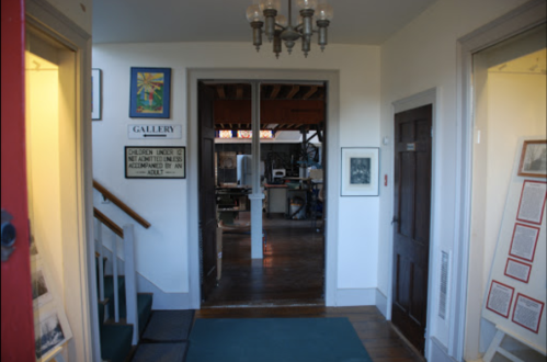 A hallway leading to a gallery, with signs and artwork on the walls, and a glimpse of a workspace beyond.