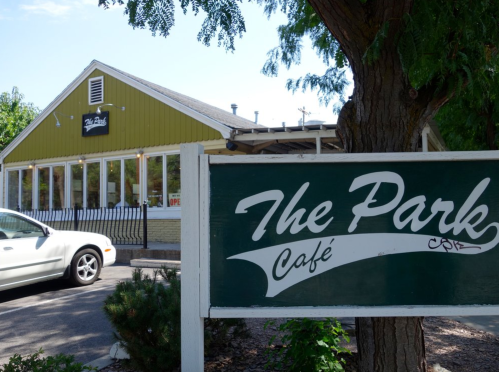 A green and white sign for "The Park Café" in front of a charming café building with large windows.