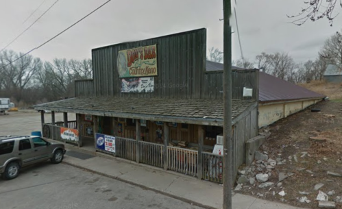 A rustic building with a wooden facade and a sloped roof, featuring signs and a porch, set in a rural area.