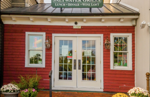 Exterior of Salt Water Grille with a red wooden facade, double doors, and colorful flower pots at the entrance.