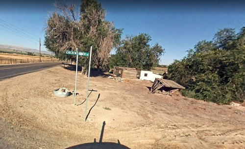 A rural scene featuring a dirt road, a street sign for "Cracked Barrel," and a dilapidated structure among trees.