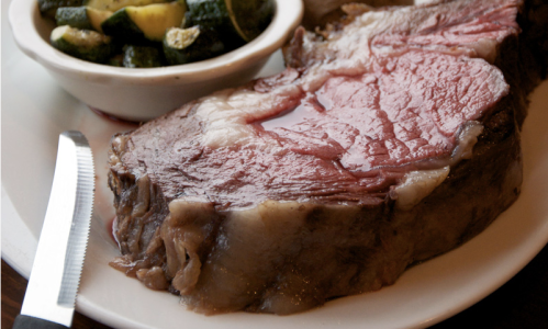 A juicy slice of prime rib served with a side of sautéed zucchini and squash on a white plate.
