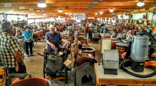 A vintage machinery exhibit with visitors exploring various antique appliances and equipment in a spacious hall.