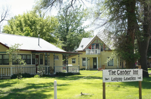 A charming inn with yellow buildings and a sign reading "The Gander Inn" surrounded by green trees and grass.