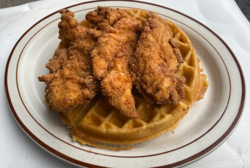 A plate of crispy fried chicken strips on top of a golden waffle.