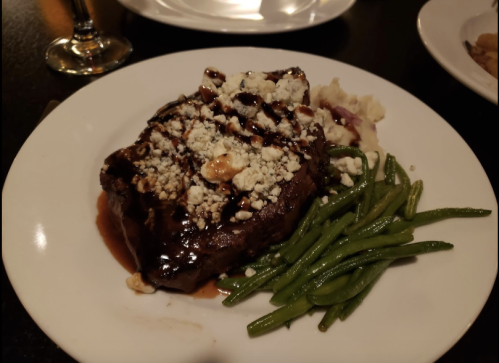 A plate featuring a steak topped with blue cheese, served with mashed potatoes and green beans.
