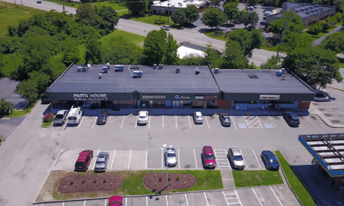 Aerial view of a restaurant plaza with the Pasta House and several parked cars in the lot. Green trees in the background.