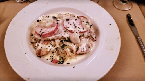 A plate of creamy seafood pasta topped with shrimp, scallops, and sliced tomatoes, garnished with parsley.