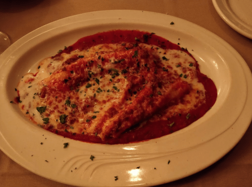 A plate of baked pasta with marinara sauce, melted cheese, and sprinkled parsley.