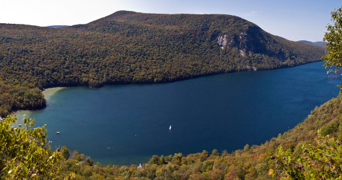 A scenic view of a lake surrounded by colorful autumn foliage and hills under a clear blue sky.