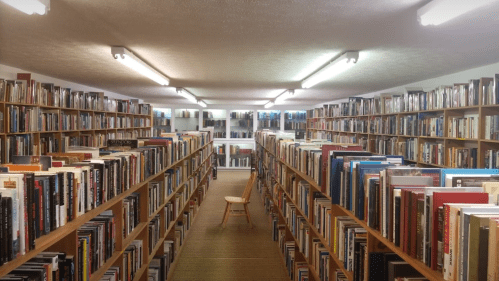 A spacious library aisle lined with bookshelves, featuring a single wooden chair in the center.