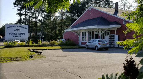 A red building with a sign reading "Douglas N. Harding Books, Maps, Prints" and a white car parked outside.