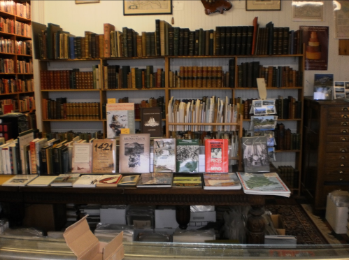 A cozy bookstore interior with shelves of books and a table displaying various titles and publications.