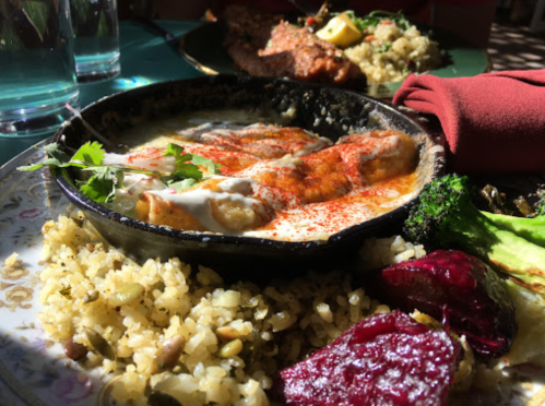 A skillet with enchiladas topped with sauce, served with rice and colorful vegetables on a decorative plate.