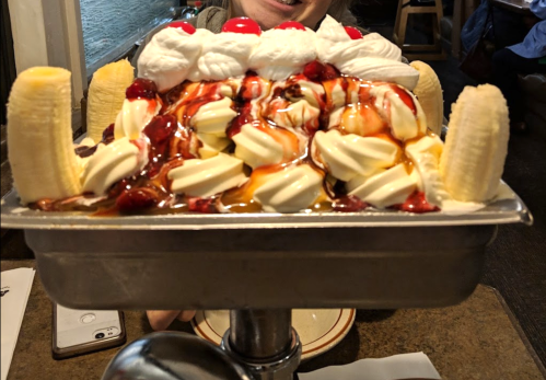 A large banana split topped with whipped cream, cherries, and chocolate syrup, served in a metal dish.