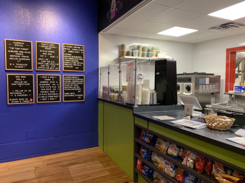 Interior of a colorful café with a menu board, counter, and snacks displayed. Brightly painted walls enhance the atmosphere.