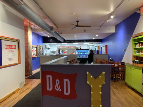 Interior of a restaurant with purple walls, a counter, and seating areas. Signage for "D&D" visible in the foreground.