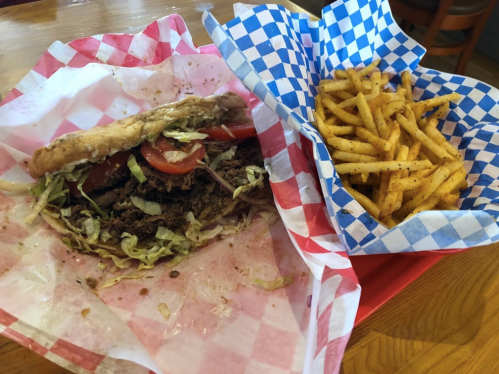 A partially eaten sandwich with lettuce and tomatoes next to a serving of golden fries in checkered paper.