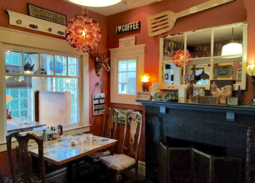 Cozy café interior with wooden tables, vintage decor, and a fireplace, featuring warm lighting and coffee-themed signs.