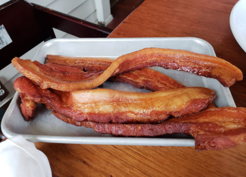 A metal tray filled with several pieces of crispy, golden-brown bacon strips on a wooden table.