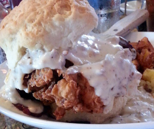 A hearty biscuit sandwich filled with fried chicken and smothered in creamy gravy, served with golden potatoes.