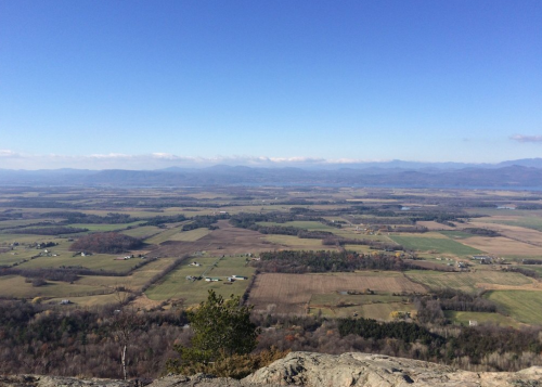 A panoramic view of rolling fields and distant mountains under a clear blue sky.