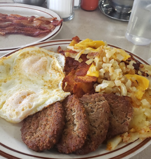 A hearty breakfast plate with two eggs, hash browns topped with cheese and onions, and sausage patties.