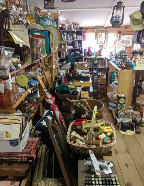 A cluttered antique shop filled with various vintage items, including toys, glassware, and decor.