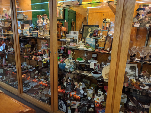 A display case filled with various antiques and collectibles, including figurines, glassware, and vintage items.