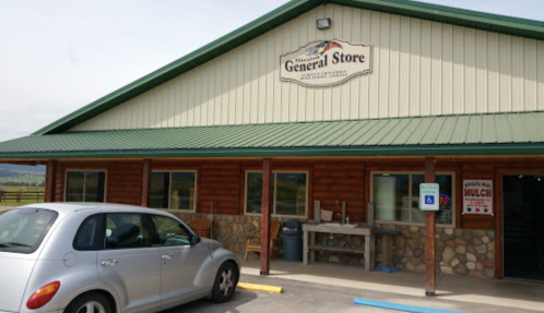 Exterior of a general store with a green roof, wooden accents, and a parked silver car in front.