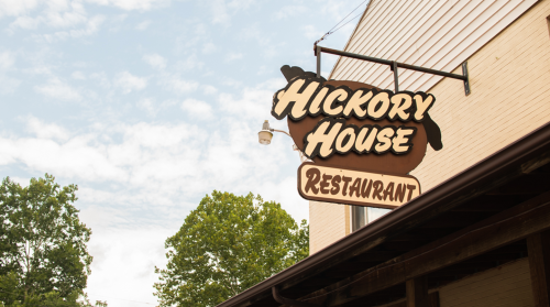 Sign for Hickory House Restaurant against a backdrop of trees and a cloudy sky.