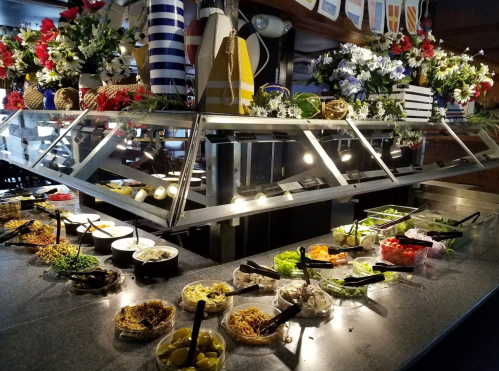 A vibrant salad bar with various toppings and garnishes, decorated with flowers and nautical-themed decor.