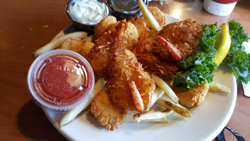 A plate of fried shrimp, fries, and a side of dipping sauces, garnished with lettuce and a lemon wedge.