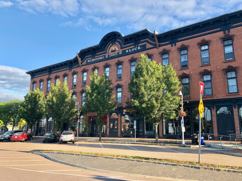 Historic brick building with "Windsor Block 1862" sign, surrounded by trees and parked cars under a blue sky.