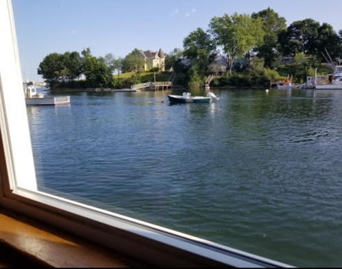 View of a calm river with boats and a house on the shore, seen through a window.