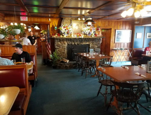 Cozy restaurant interior with wooden decor, tables, a stone fireplace, and patrons enjoying their meals.