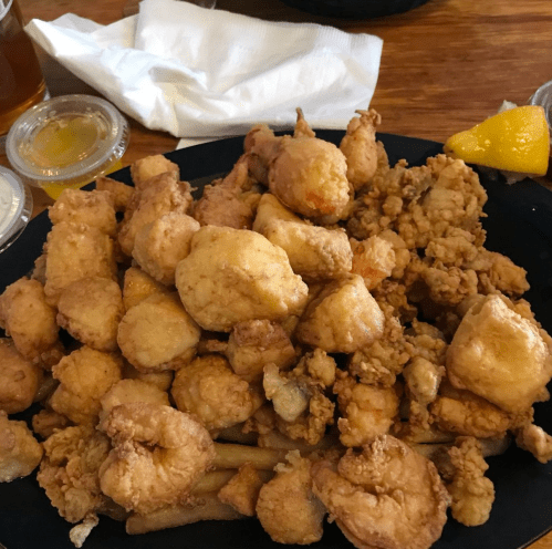A plate piled high with golden fried seafood, including shrimp and fish, served with lemon and dipping sauces.