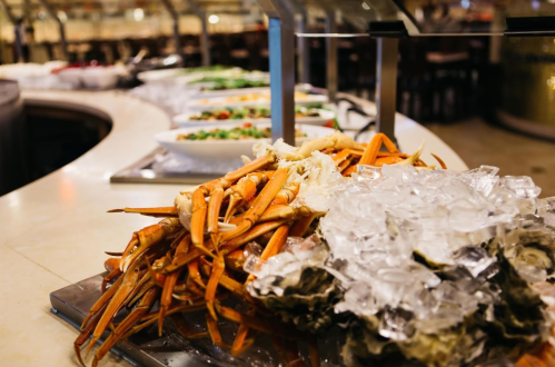 A seafood display featuring crab legs and oysters on ice, with salads in the background.