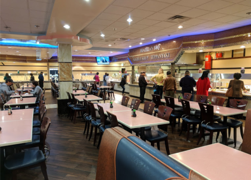A spacious restaurant interior with tables and a buffet line, featuring diners serving themselves food.