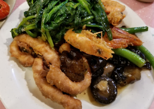 A plate of mixed seafood and vegetables, featuring fried shrimp, greens, and dark mushrooms.